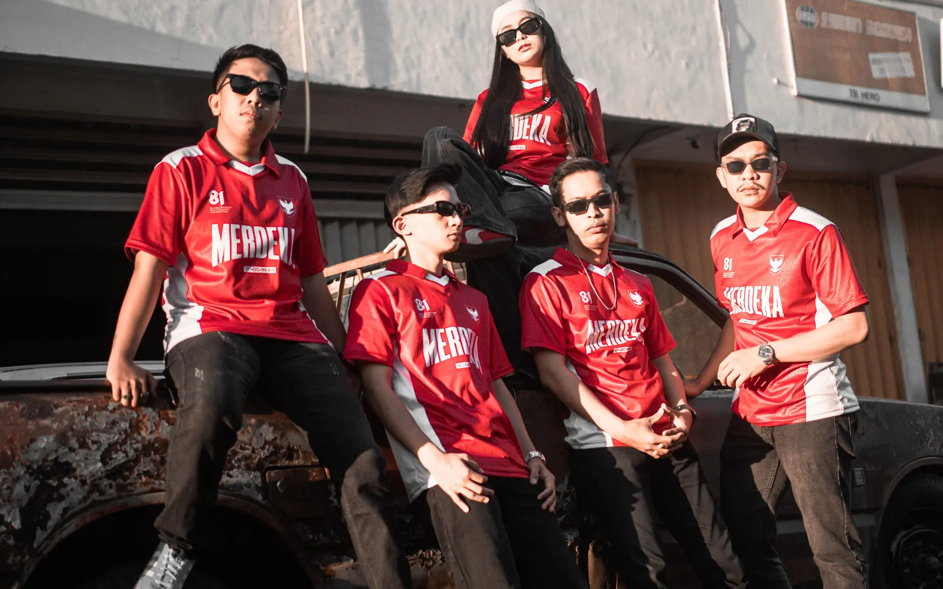 Satu tim memakai jersey Merdeka di atas mobil tua